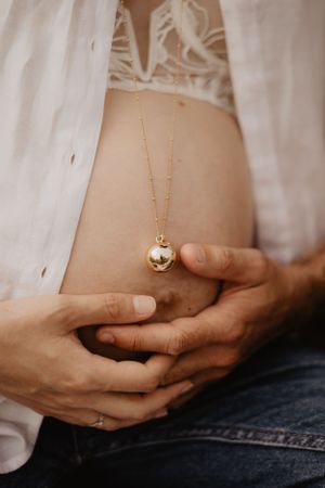 Close-up of hands tenderly cradling a pregnant belly with a delicate gold necklace.