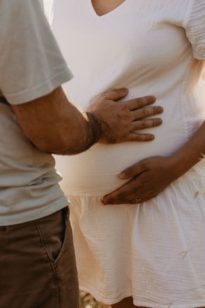 Gentle hands rest on a pregnant belly against soft white fabric.