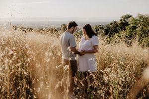 A couple stands together in a sunlit field of dry grass during golden hour.