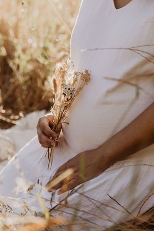 Hands holding dried flowers against white fabric in warm sunlight.