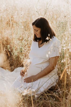 Maternity photoshoot in a sunlit field of golden dried grass.