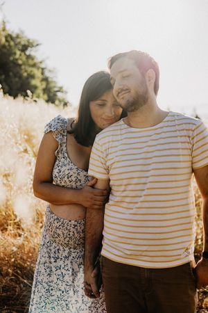 A couple embraces in golden sunlight against a natural backdrop wearing striped and floral clothing.