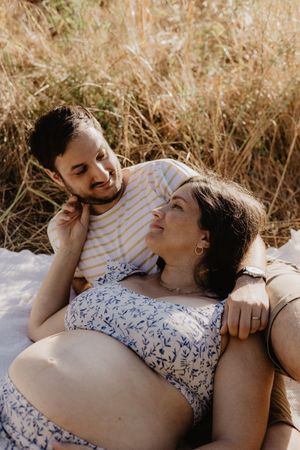 Two people lying together in tall grass during a sunny afternoon photo session.
