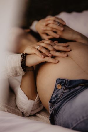 Multiple hands tenderly placed on bare skin in intimate maternity pose.