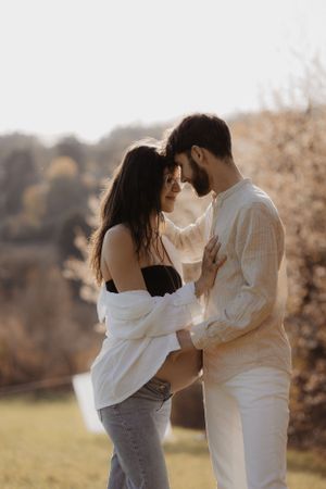 Romantic couple in white clothing embracing outdoors in warm sunlight.