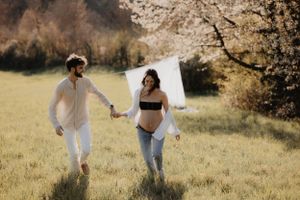 Couple walking hand in hand through sunny meadow with cherry blossoms.