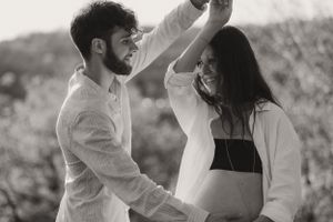 Dancing couple in white clothing share joyful moment in natural setting.