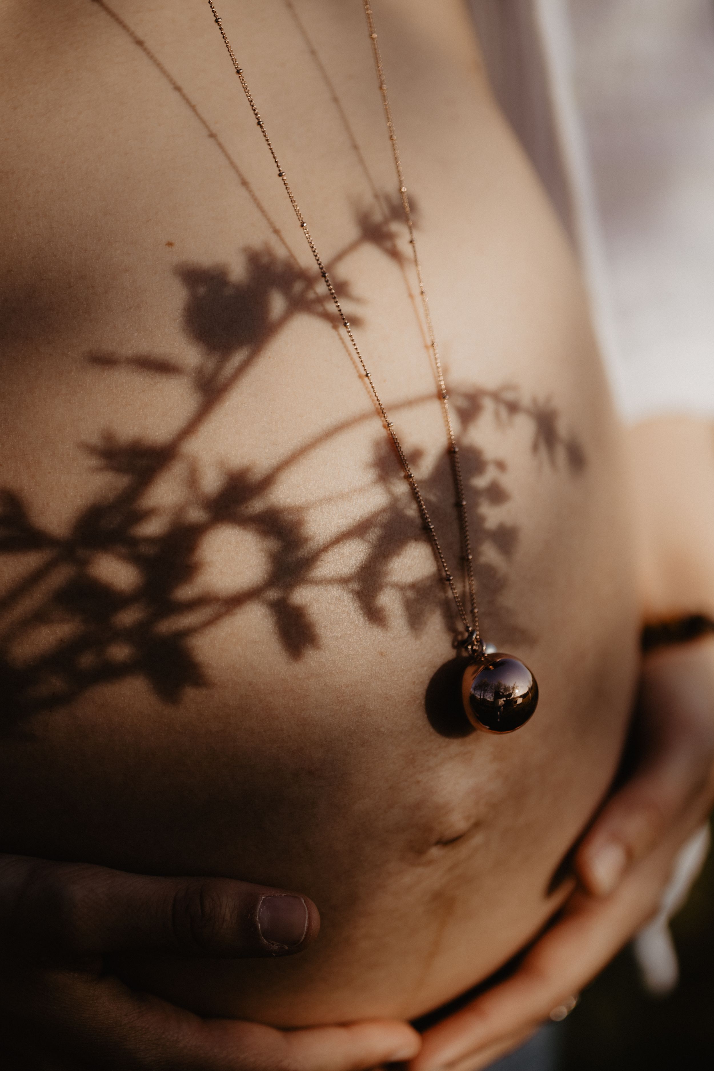 Artistic shadow of plant on pregnant belly with necklace pendant.