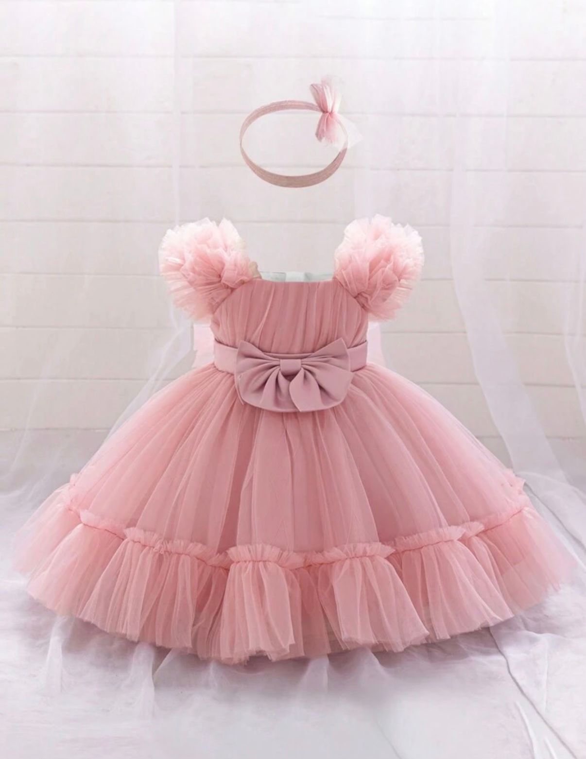 Pink tulle baby dress with bow detail and ruffled skirt perfect for special occasions.