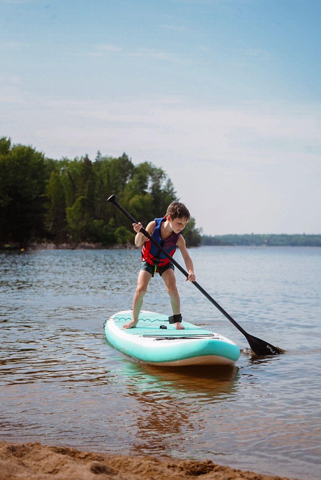 Person paddleboarding on calm lake waters near a forested shoreline.