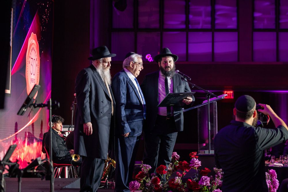 Evening event features speakers at a podium with purple stage lighting and floral decorations.