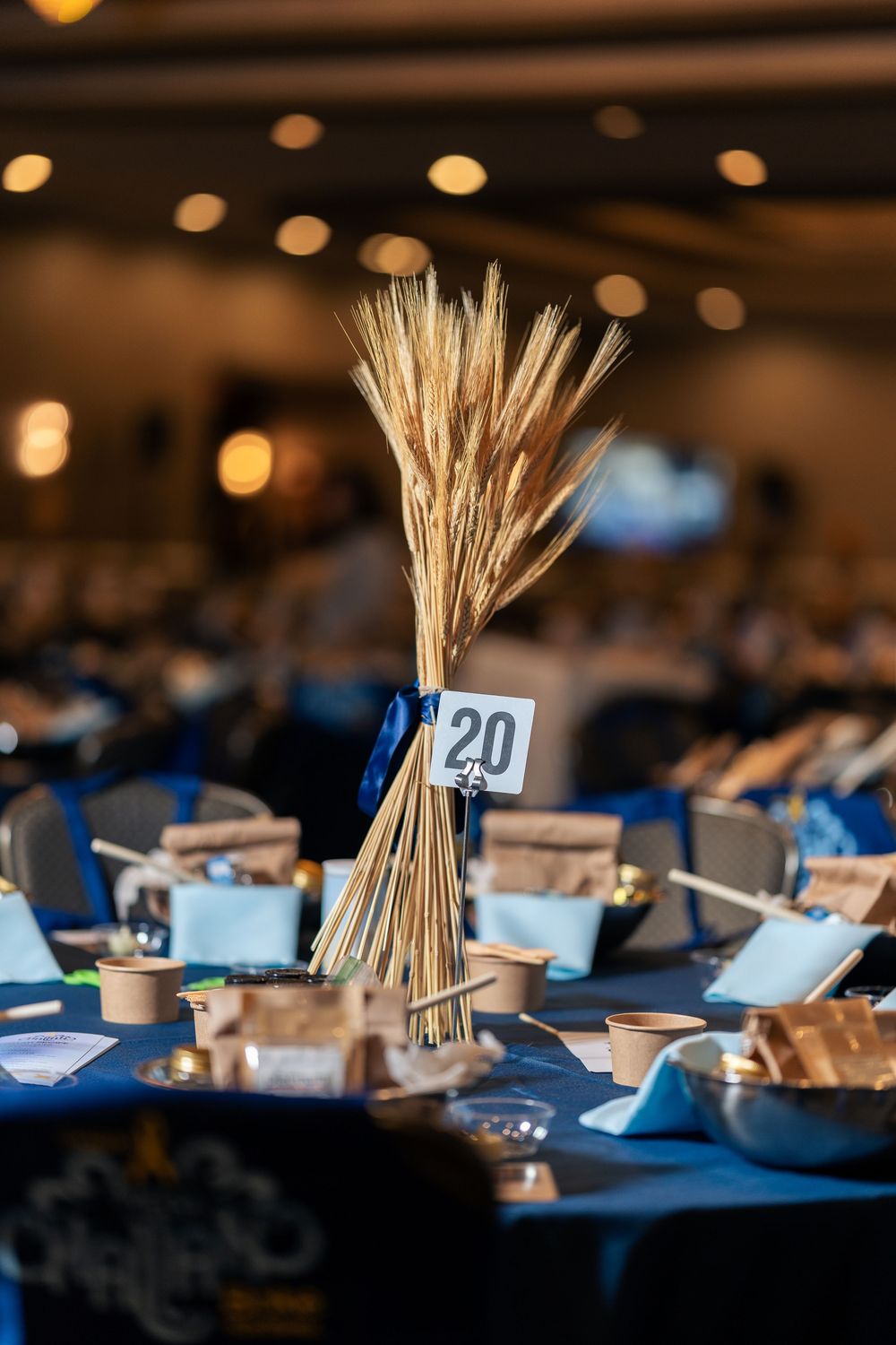 A rustic wedding centerpiece with wheat stalks and table number 20 on a navy blue tablecloth.