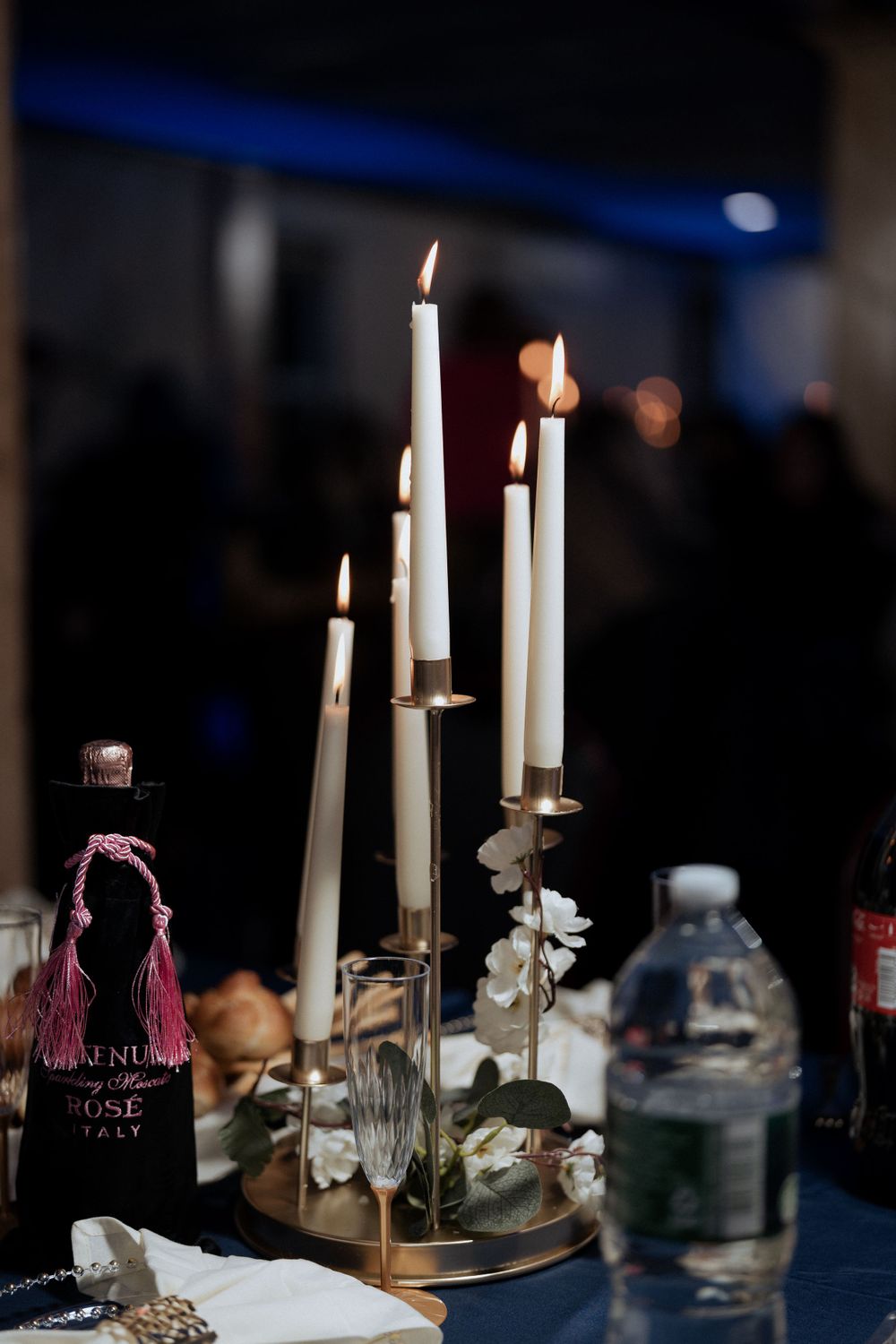 Elegant table setting with lit white candles in gold holders and decorative bottle.