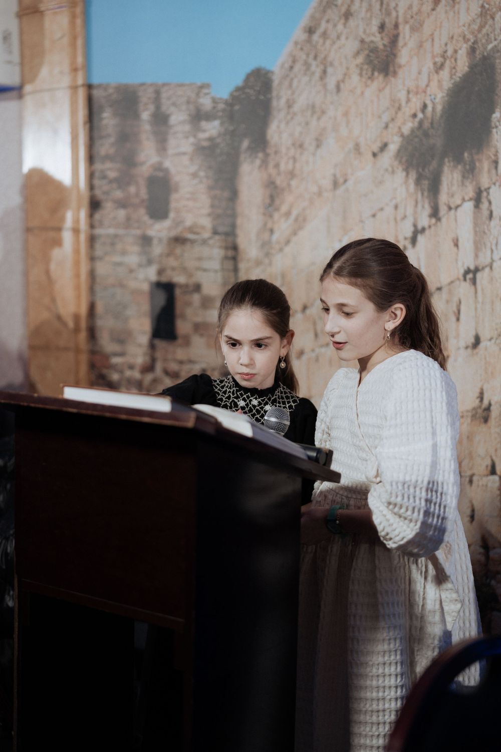 Two musicians performing together beside an ancient stone wall in a moody artistic setting.