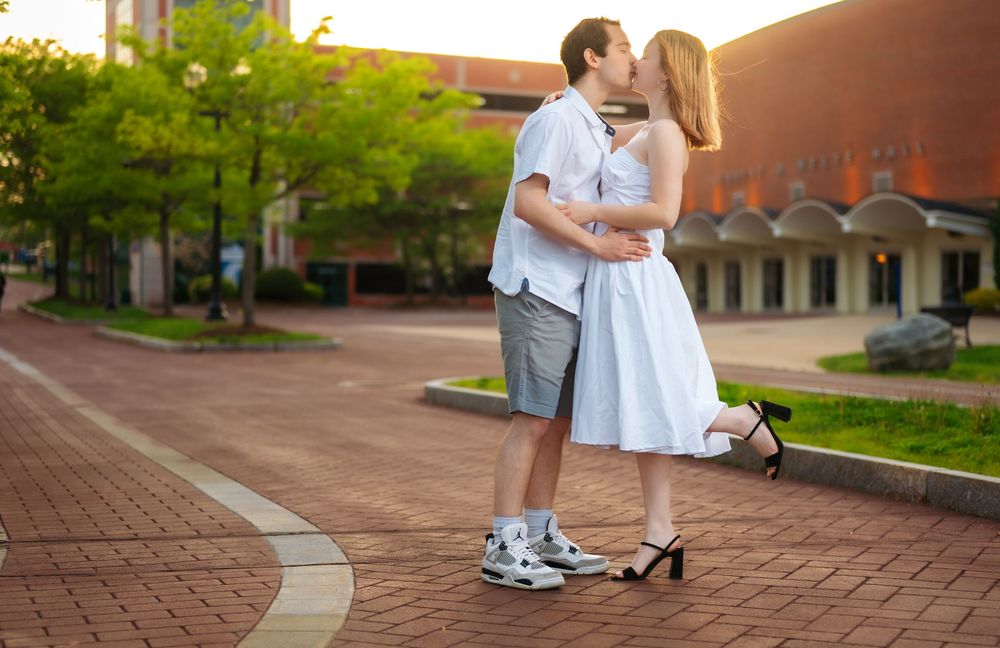 A couple poses together on a brick walkway during sunset near campus buildings.