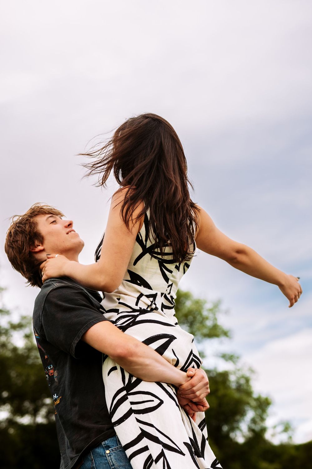 A couple spins and dances together joyfully in an outdoor setting against a cloudy sky.