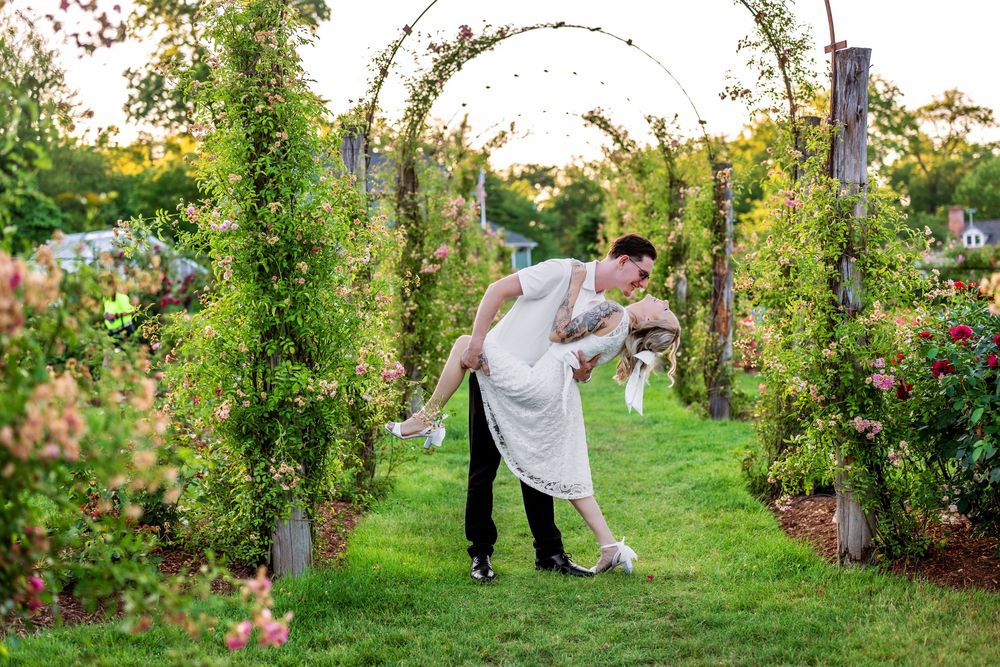 A couple shares a romantic dance pose in a garden archway filled with climbing vines and flowers.