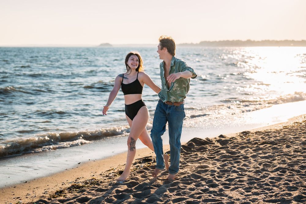 A couple runs playfully along the beach shoreline at sunset.