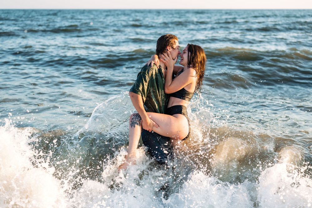 A couple embraces in ocean waves during sunset creating a romantic splash.