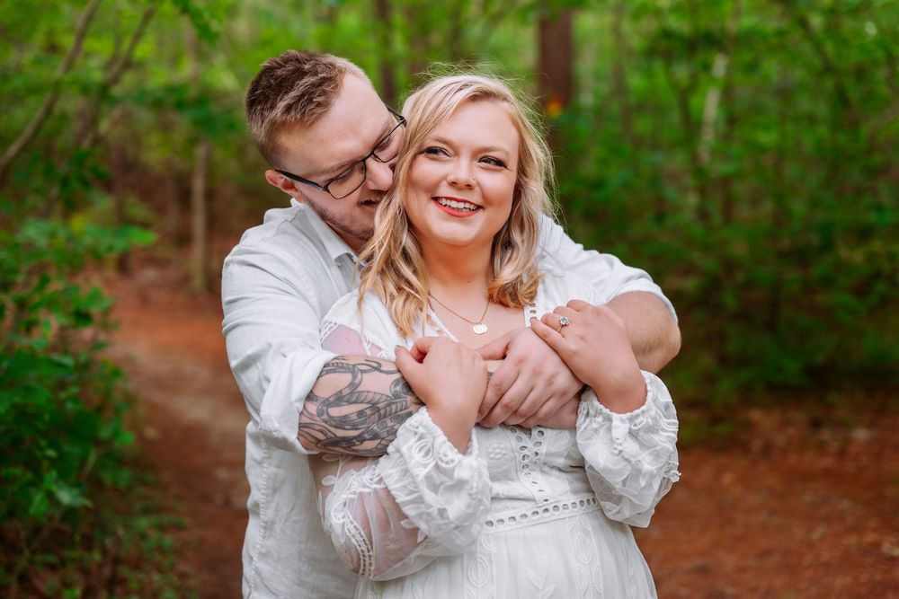 A romantic outdoor photoshoot with a couple in white clothing against green foliage.