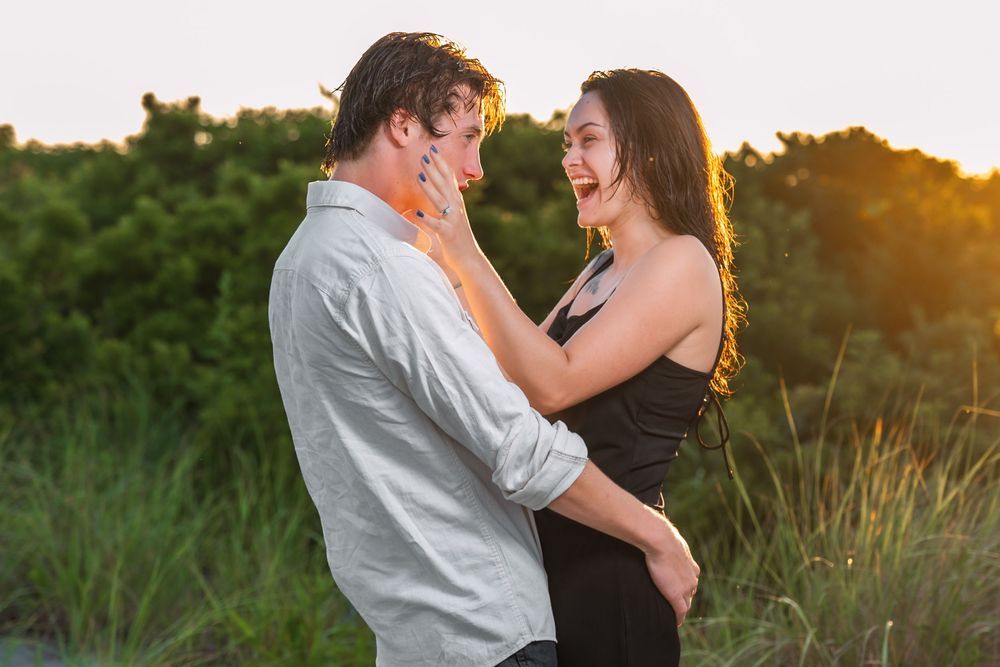 A couple shares an intimate moment against a sunset backdrop with coastal vegetation.
