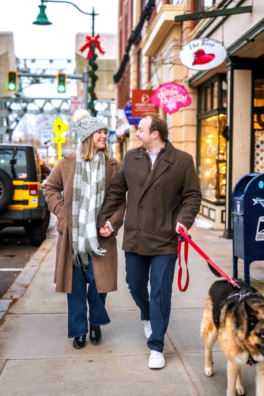 Couple walking their dog along a festive winter street with holiday decorations.
