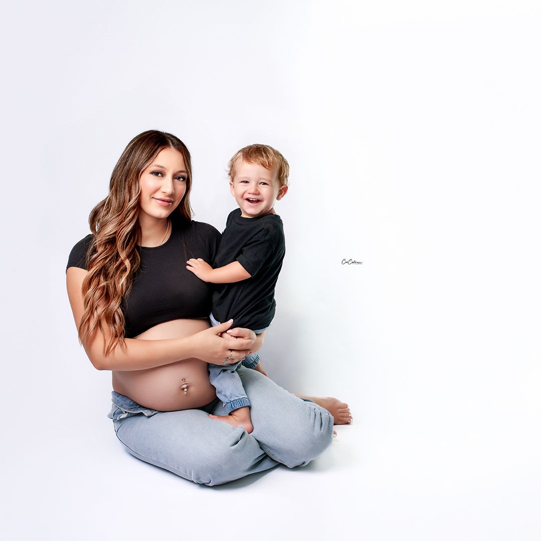 Soft light on a mother and son in matching jeans and black t-shirts on white backdrop, intimate studio photo.