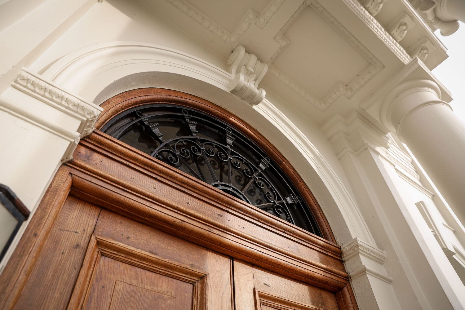 Ornate architectural detail of a grand wooden door with arched window and white crown molding.