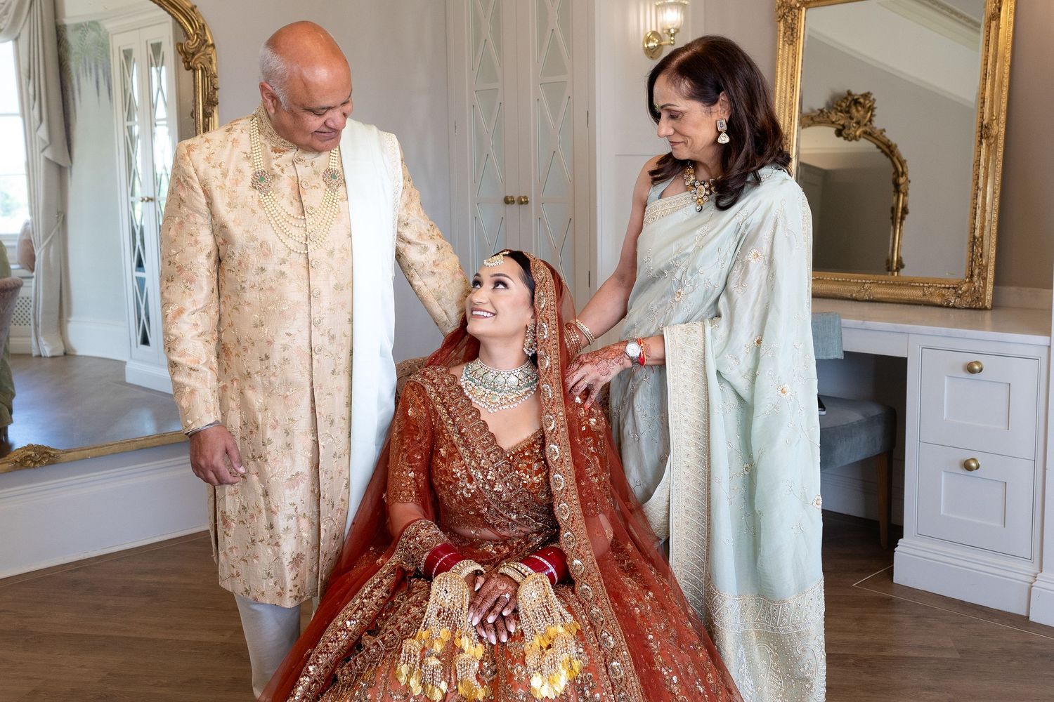 Traditional South Asian wedding preparation scene in an elegant room with ornate furniture and mirrors.