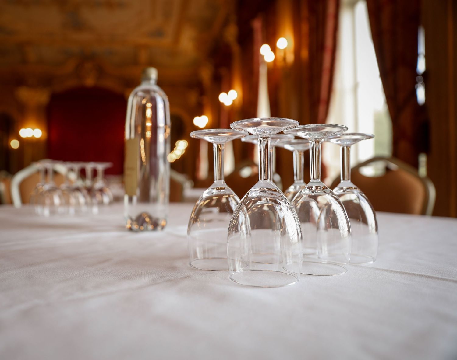 Wine glasses arranged upside down on an elegant white tablecloth with candlelight in a formal dining room.