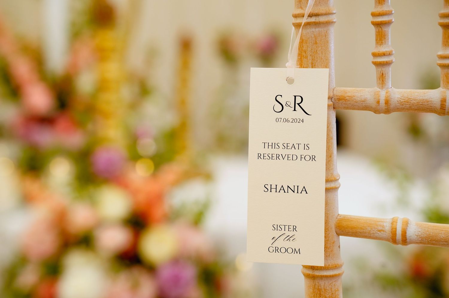 Wedding seating card displayed on a bamboo chair with floral decorations in the background.