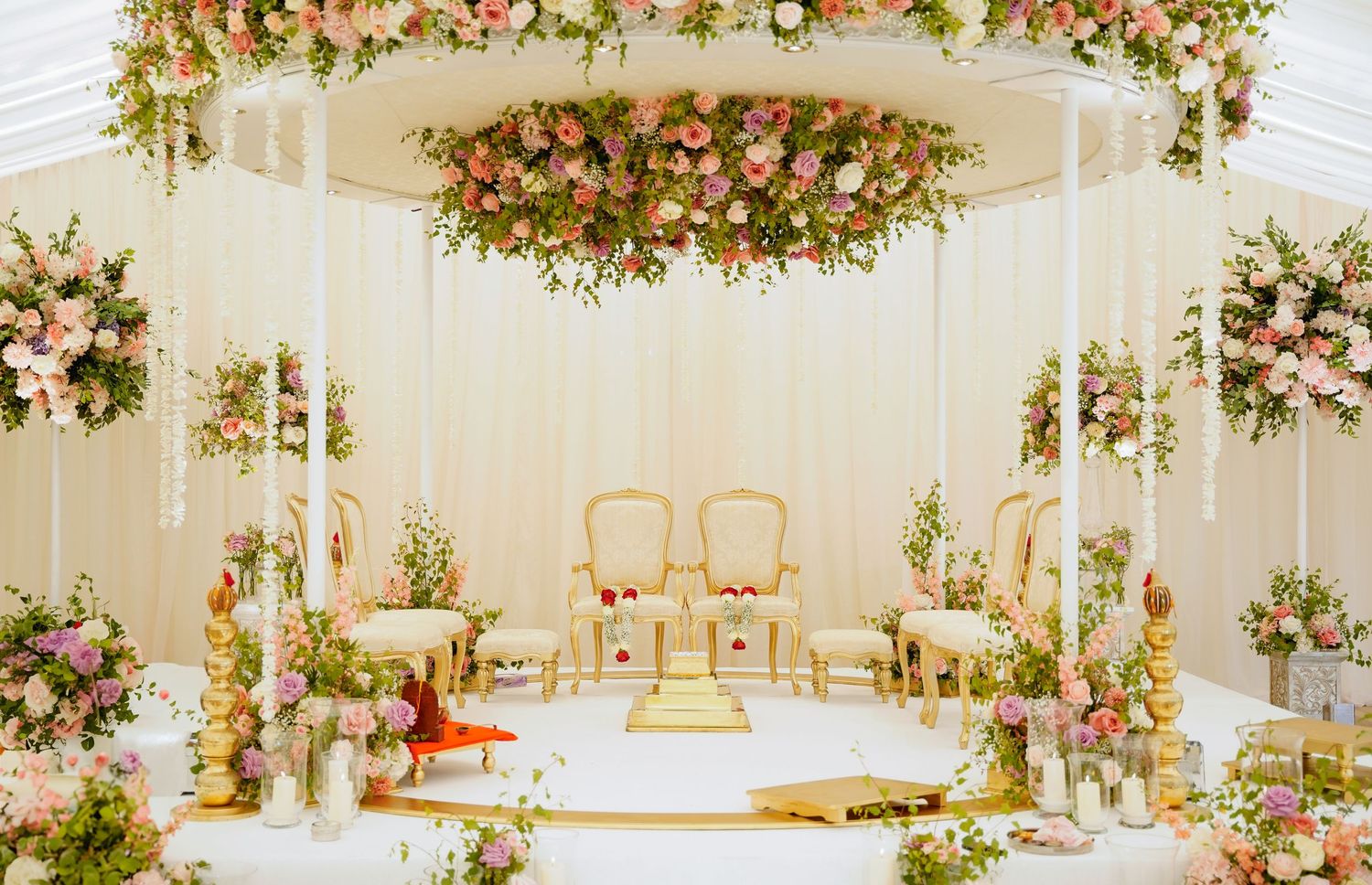 Elegant white wedding mandap decorated with pink and peach floral arrangements and hanging decor elements.