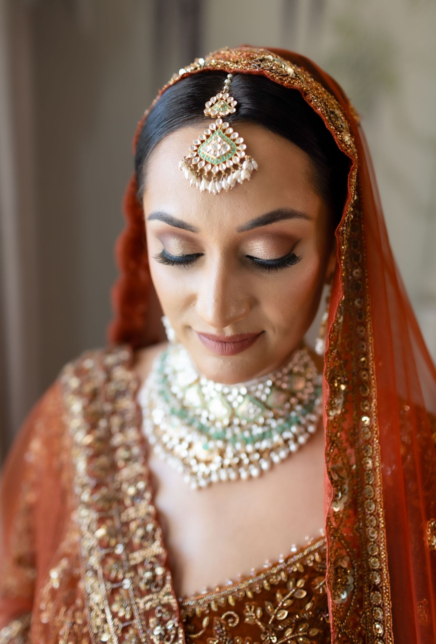 Close up of traditional Indian bridal jewelry and makeup with intricate gold and green details.