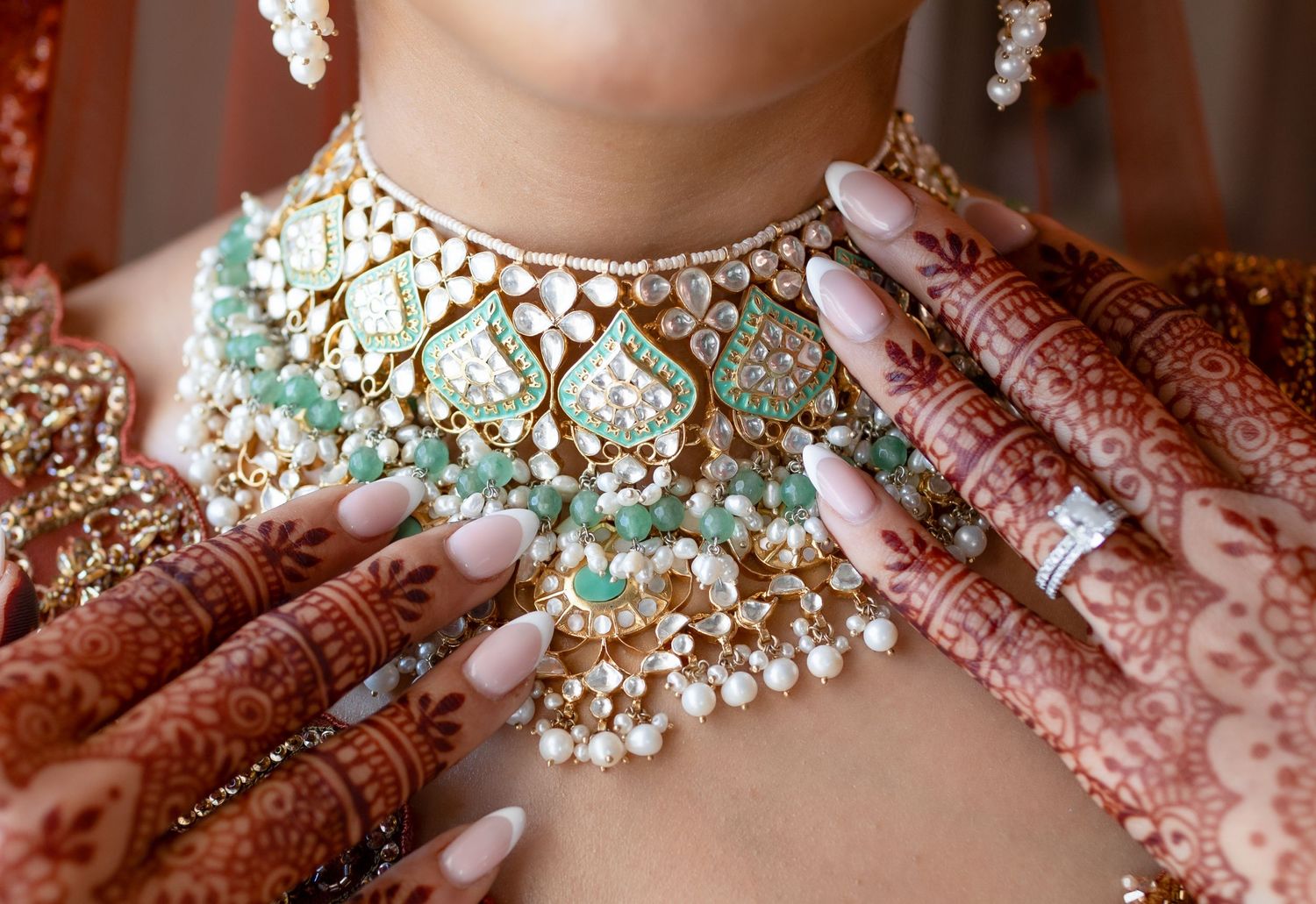Ornate gold and turquoise wedding necklace with pearls shown with traditional henna-decorated hands.
