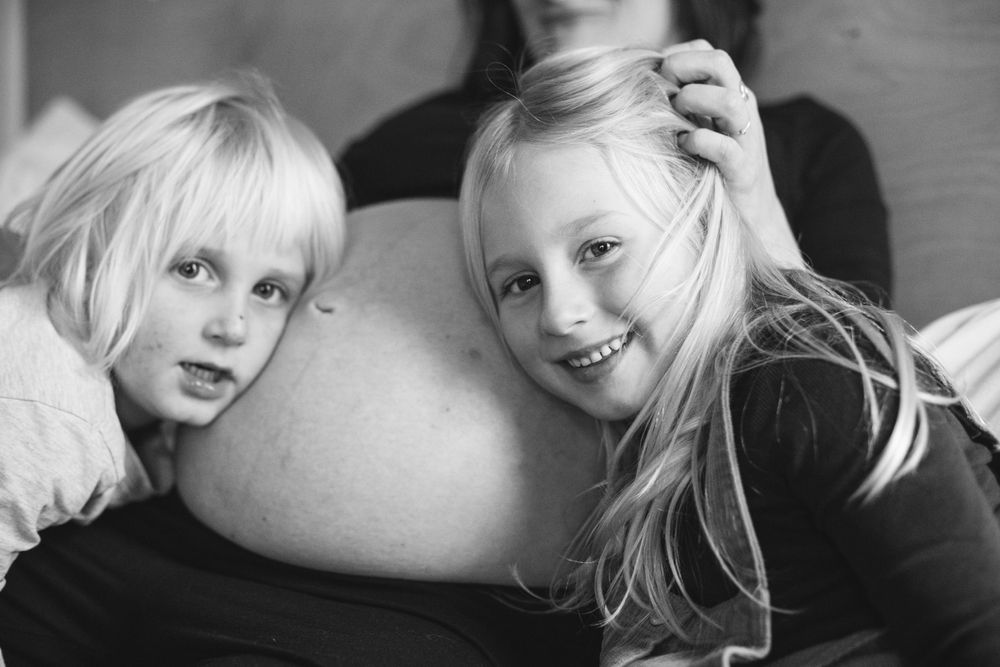 Black and white photo of two children smiling while leaning on a couch cushion together.