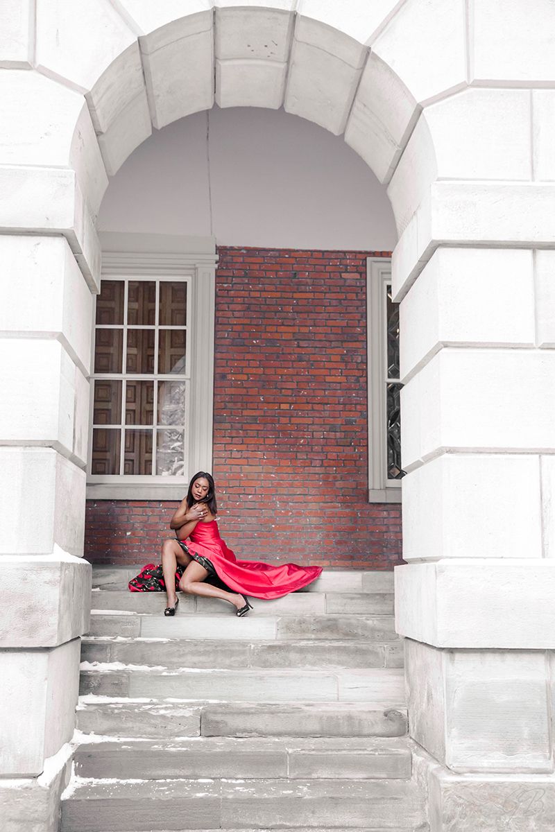 Dramatic architectural photo featuring a flowing red dress against white stone columns and brick walls.