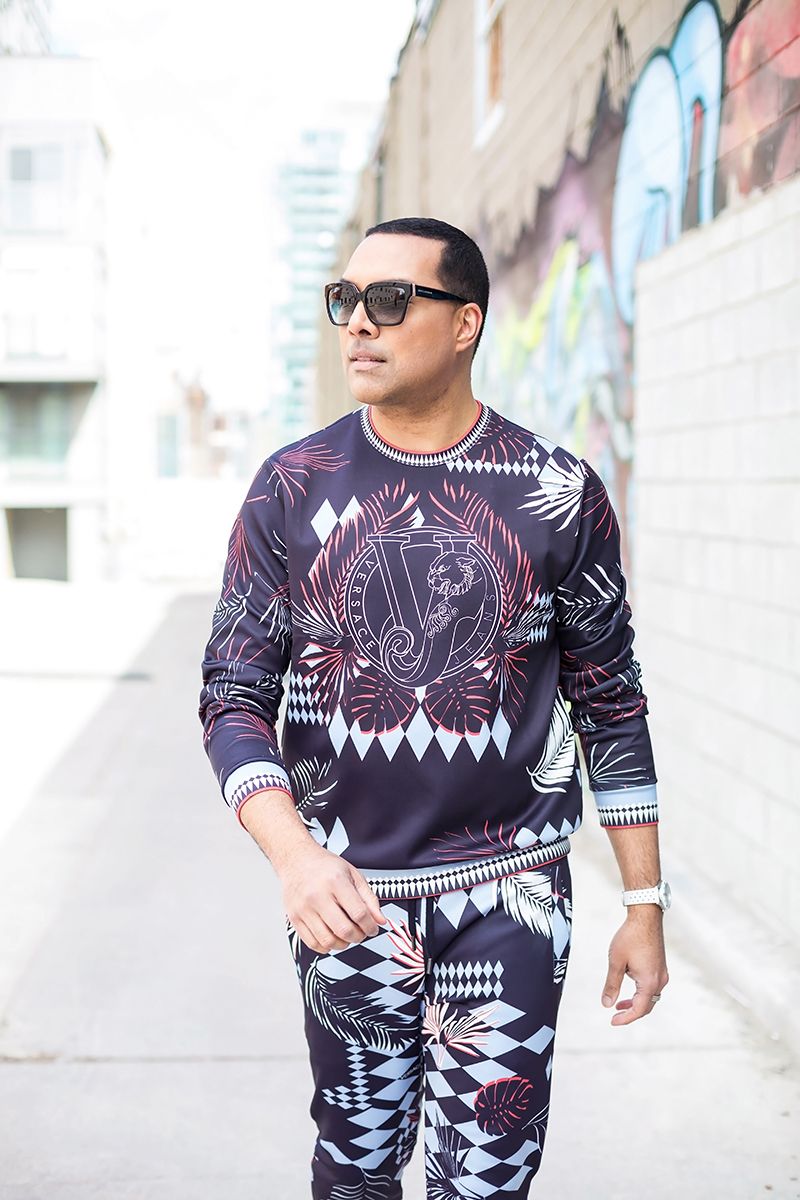 Street fashion photo of model wearing geometric print matching sweatshirt and pants against urban wall.