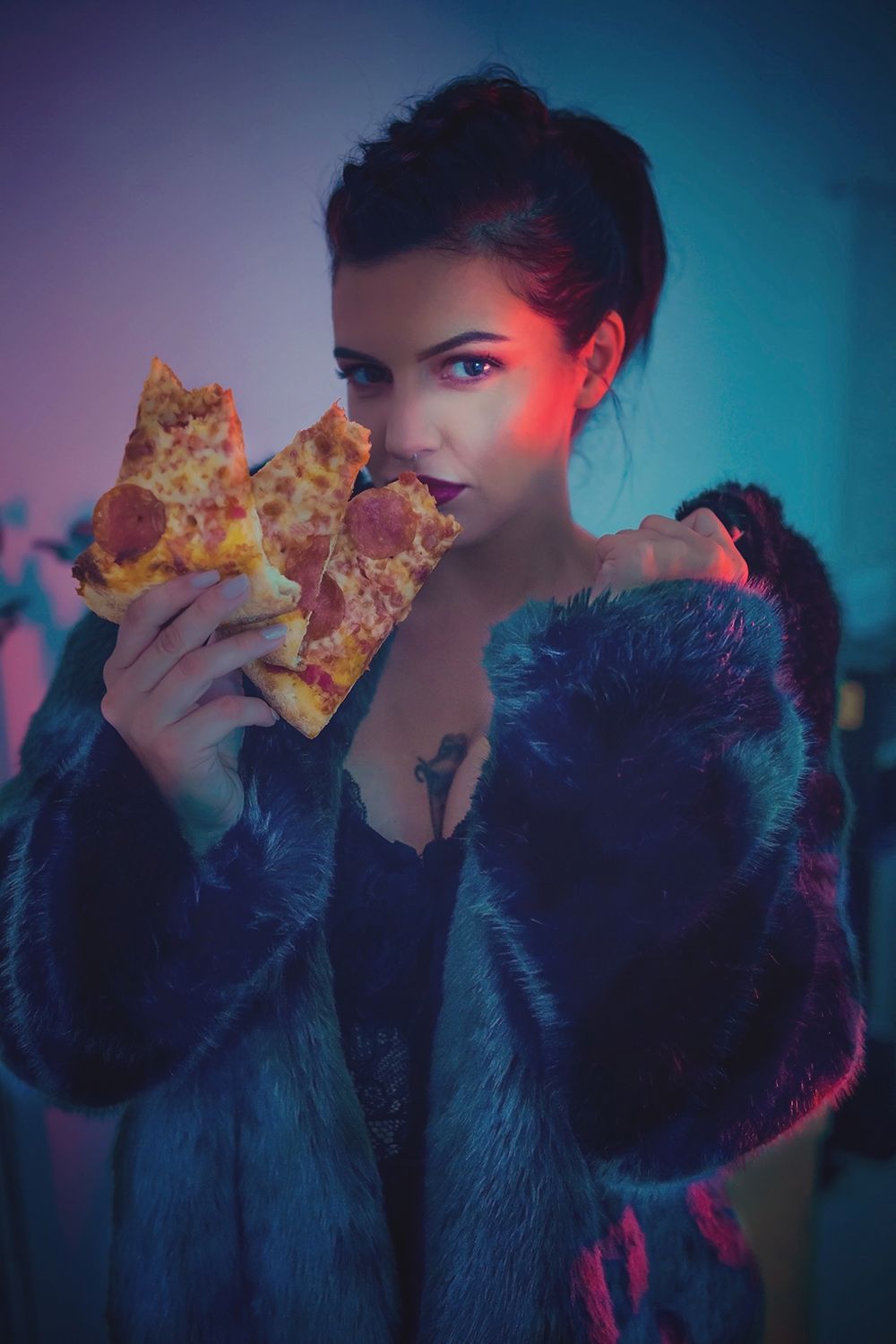 Stylish portrait with neon lighting showing person eating pizza while wearing a faux fur coat.