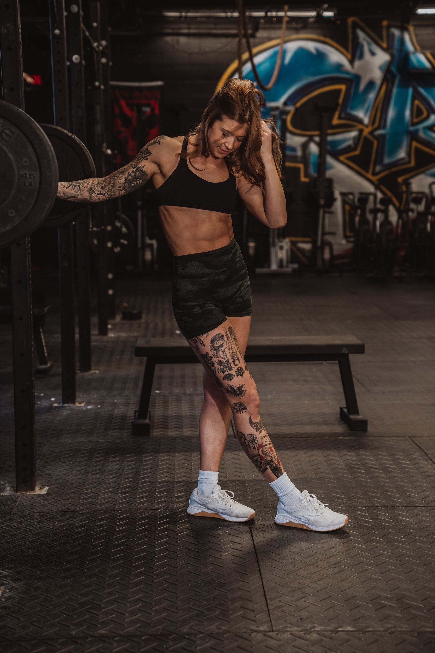Person in athletic wear shows leg tattoo while sitting in modern gym setting.