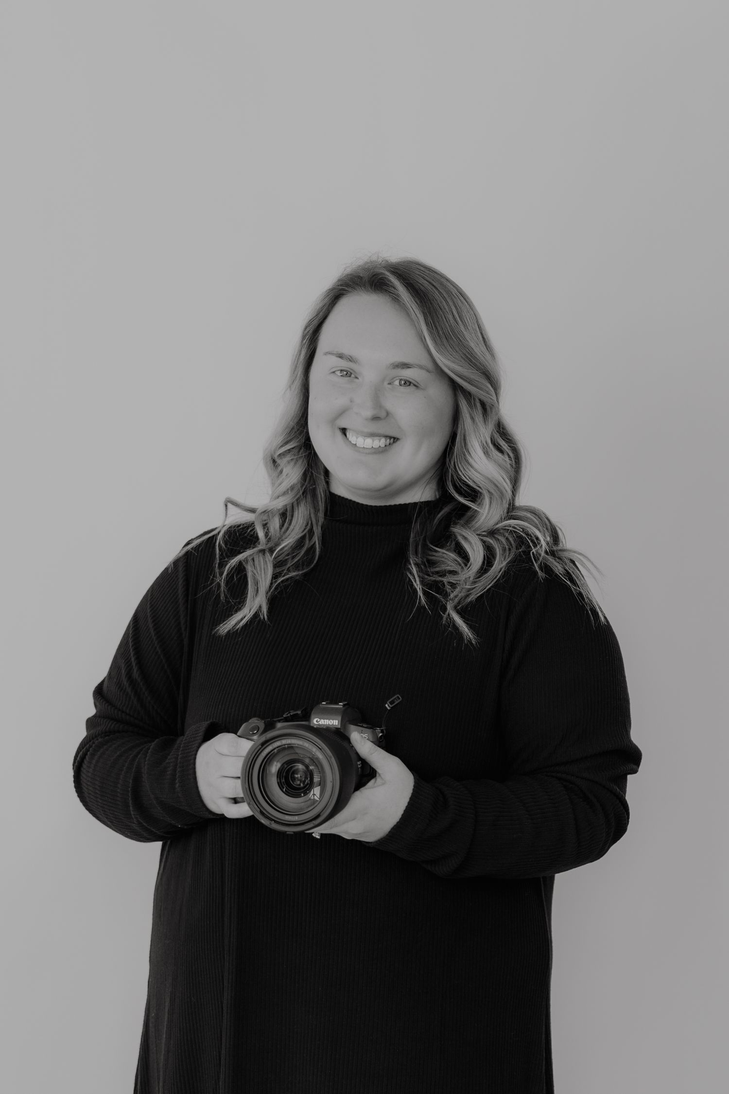 Professional photographer in black sweater holding DSLR camera in studio portrait.