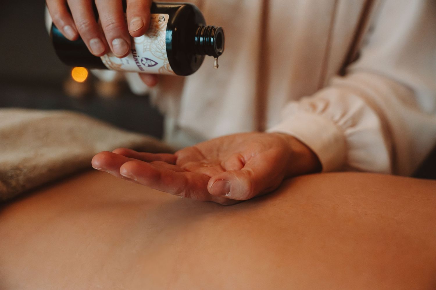 Massage therapist pours oil into palm before performing therapeutic massage treatment.