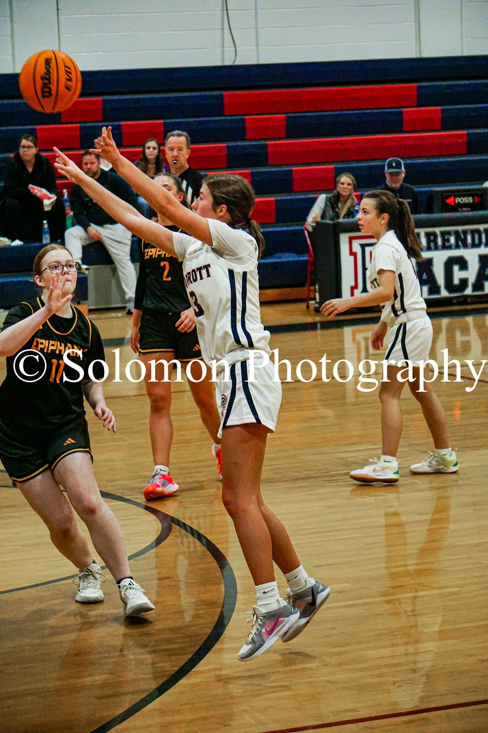 Girls basketball players compete for rebound during high school game in blue and black uniforms.