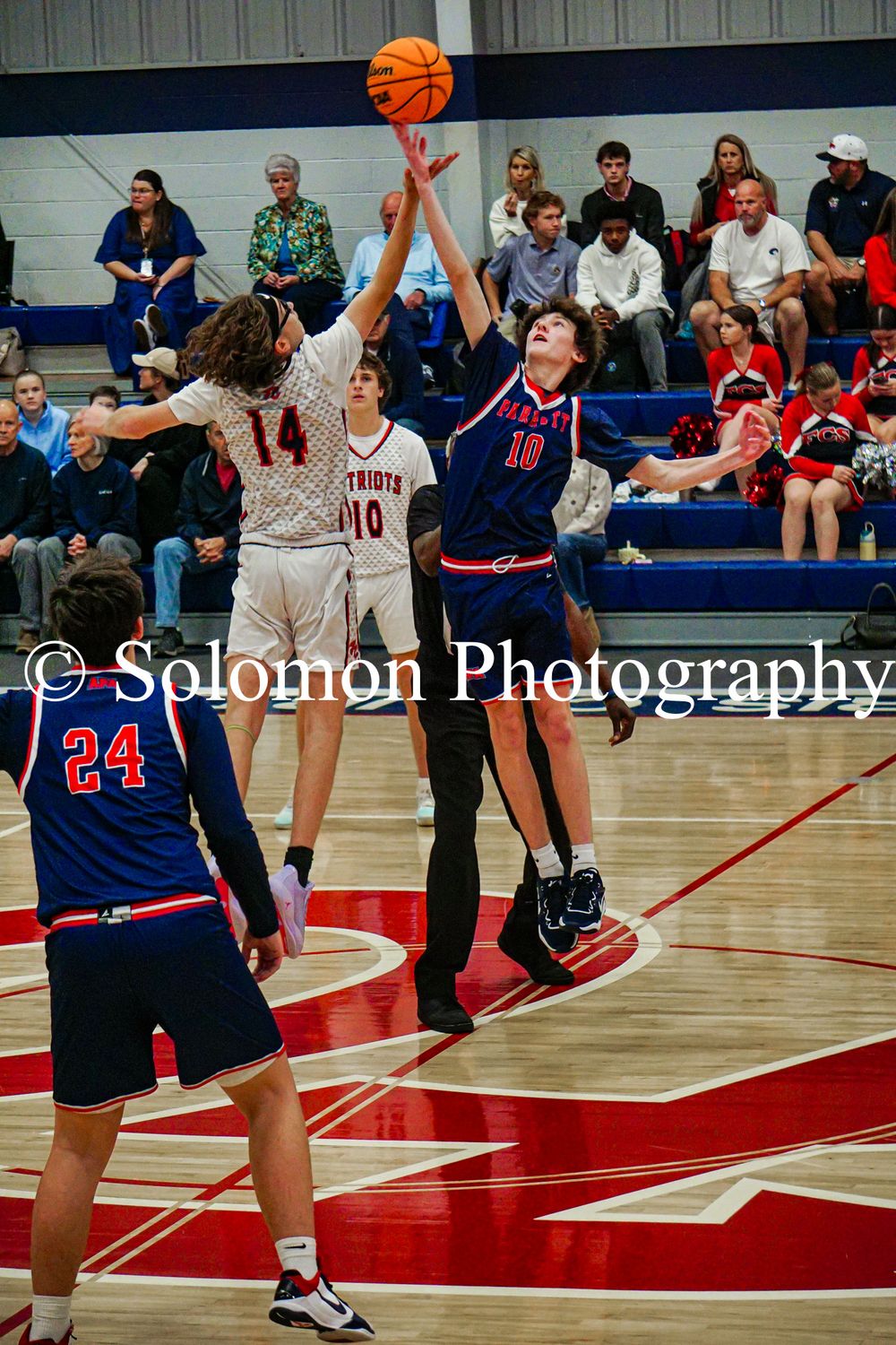 Players jump for tip-off at center court during boys high school basketball game.