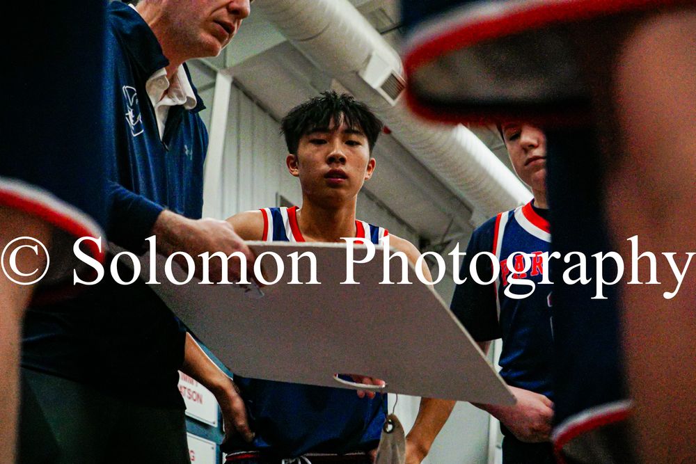 Coach reviews plays on whiteboard with players during high school basketball huddle.