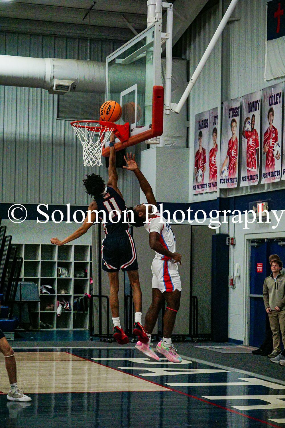 Two players battle for rebound near basket during high school boys basketball game.
