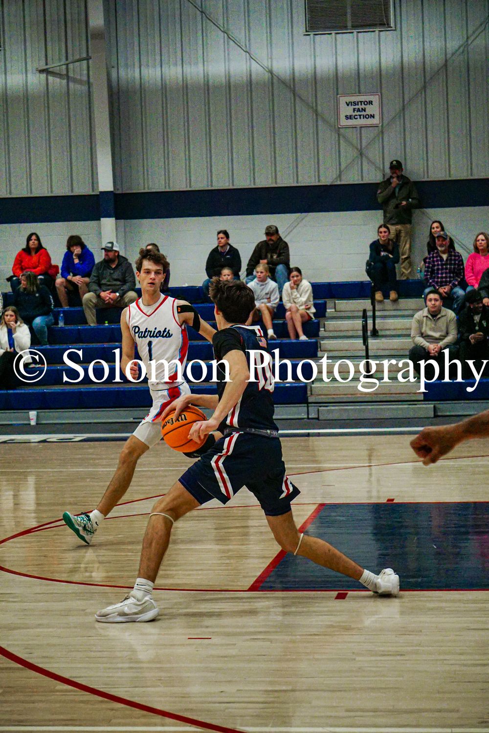 Patriots player dribbles ball while defended during high school boys basketball game.