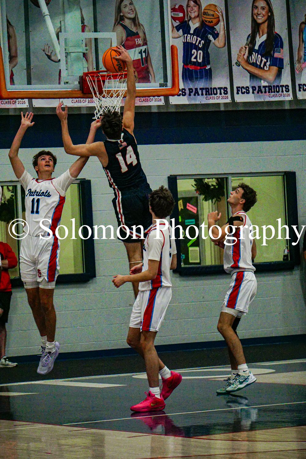 Player #14 dunks over Patriots defenders during high school boys basketball game.
