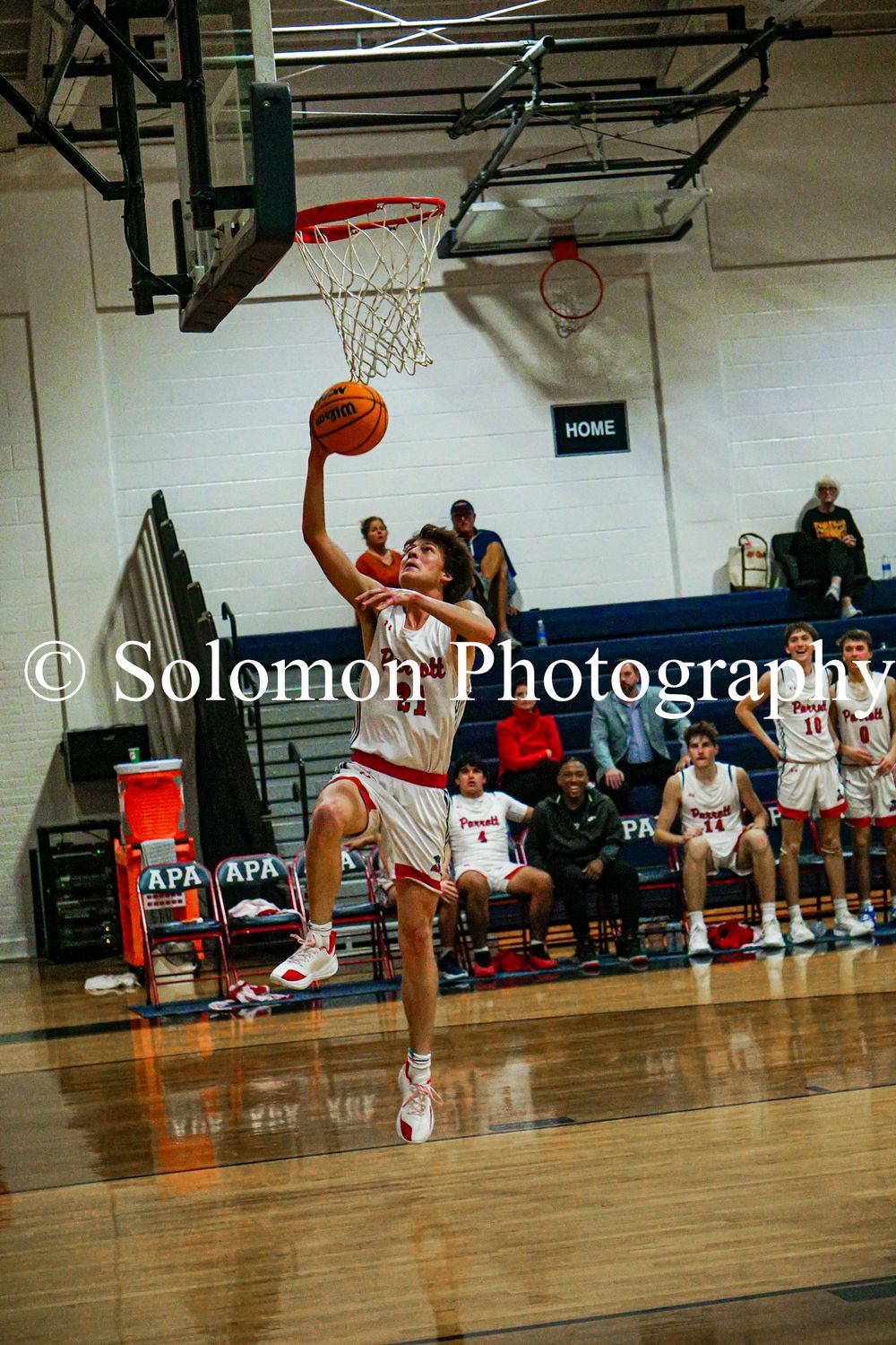A basketball player in white uniform goes up for a layup during a high school game at the APA gymnasium.