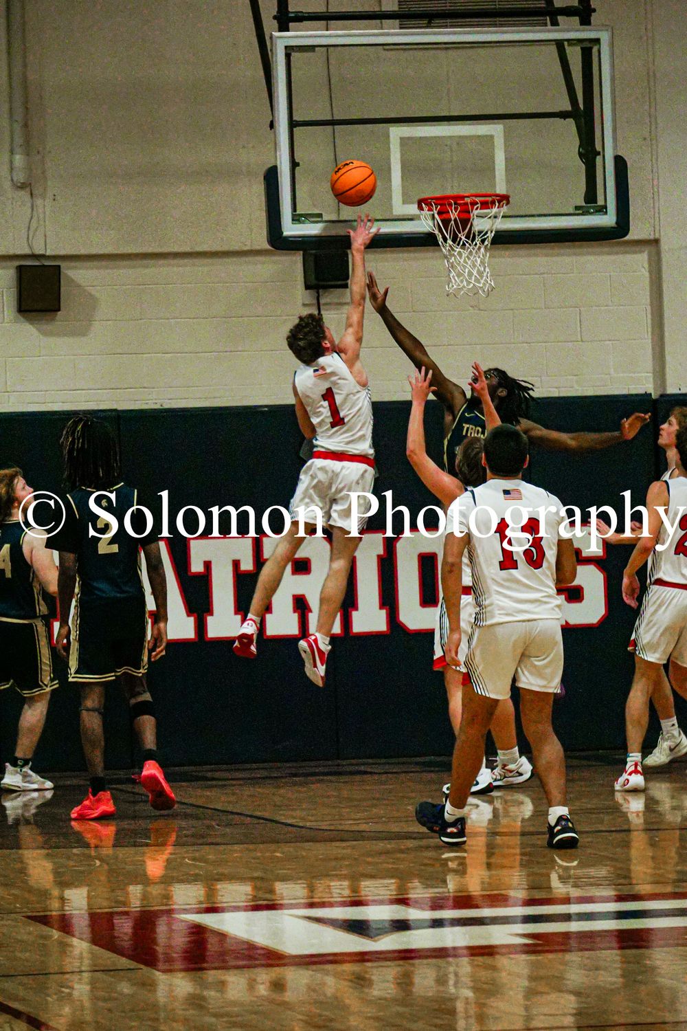 Player number 1 in white attempts a layup against a defender during a high school basketball game.