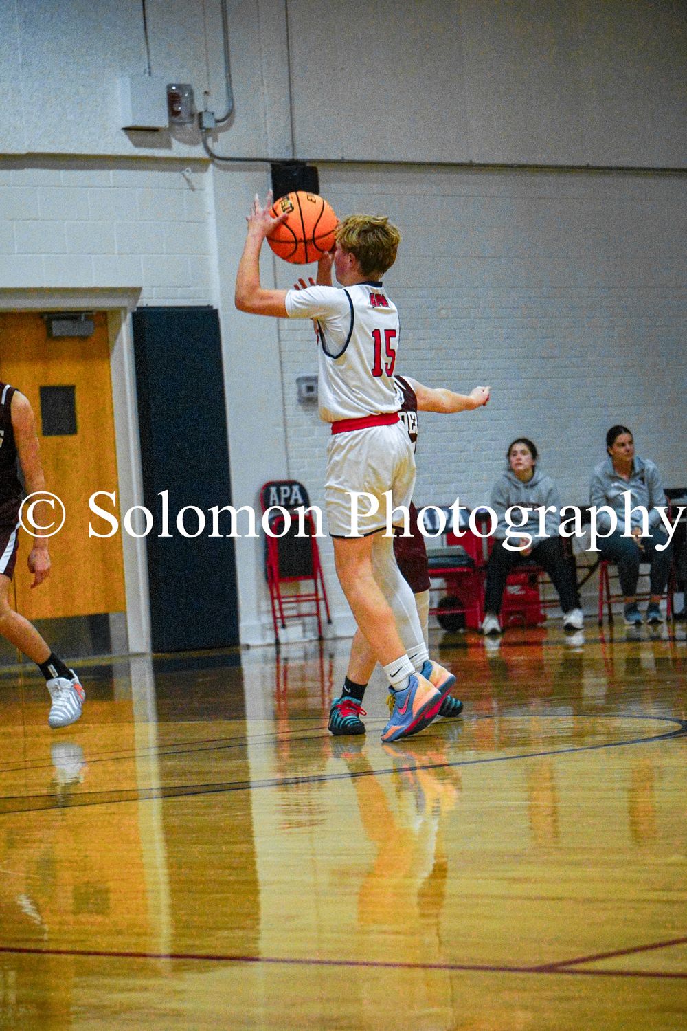 A basketball player wearing number 15 shoots a jump shot from the perimeter during a high school game.
